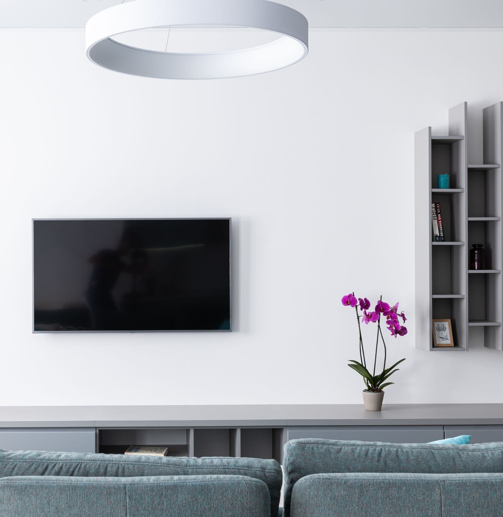 A media wall with a mounted television, built-in gray console, and geometric wall shelving styled as one design