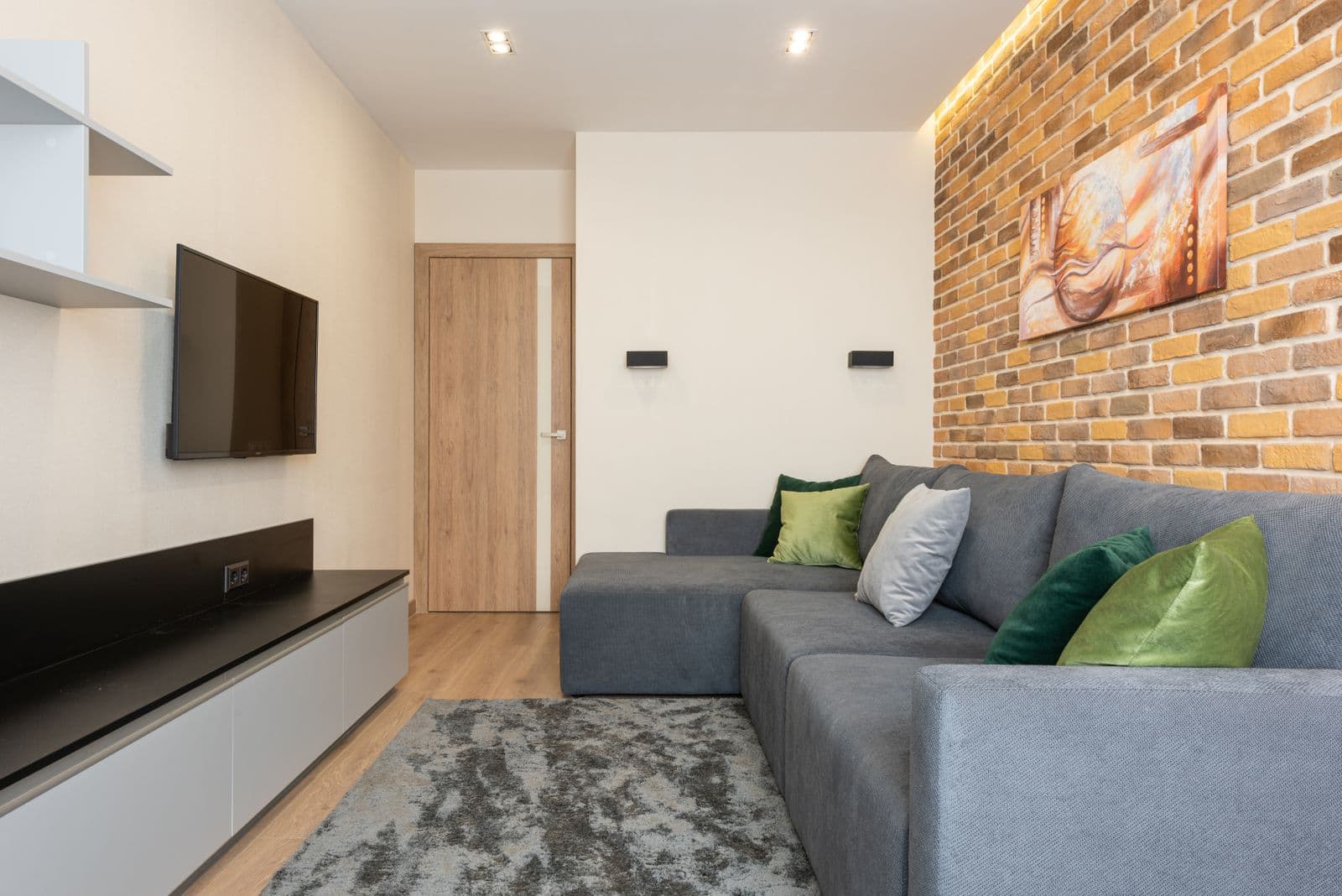 A living room with a brick accent wall, mounted television, and hung canvas art